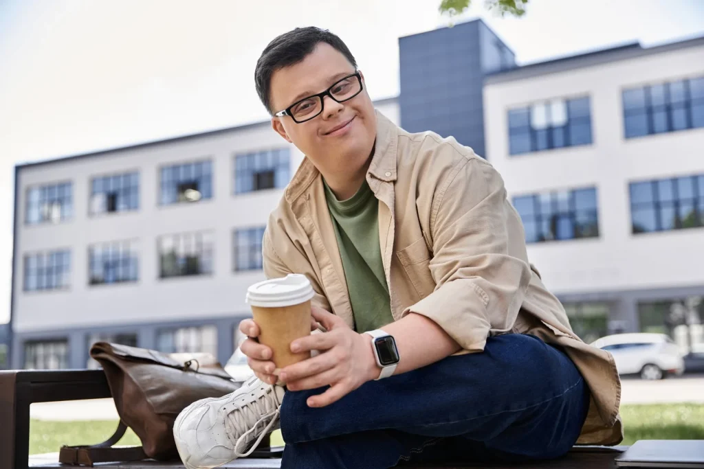 Disabled man with down syndrome holding coffee and smiling at camera